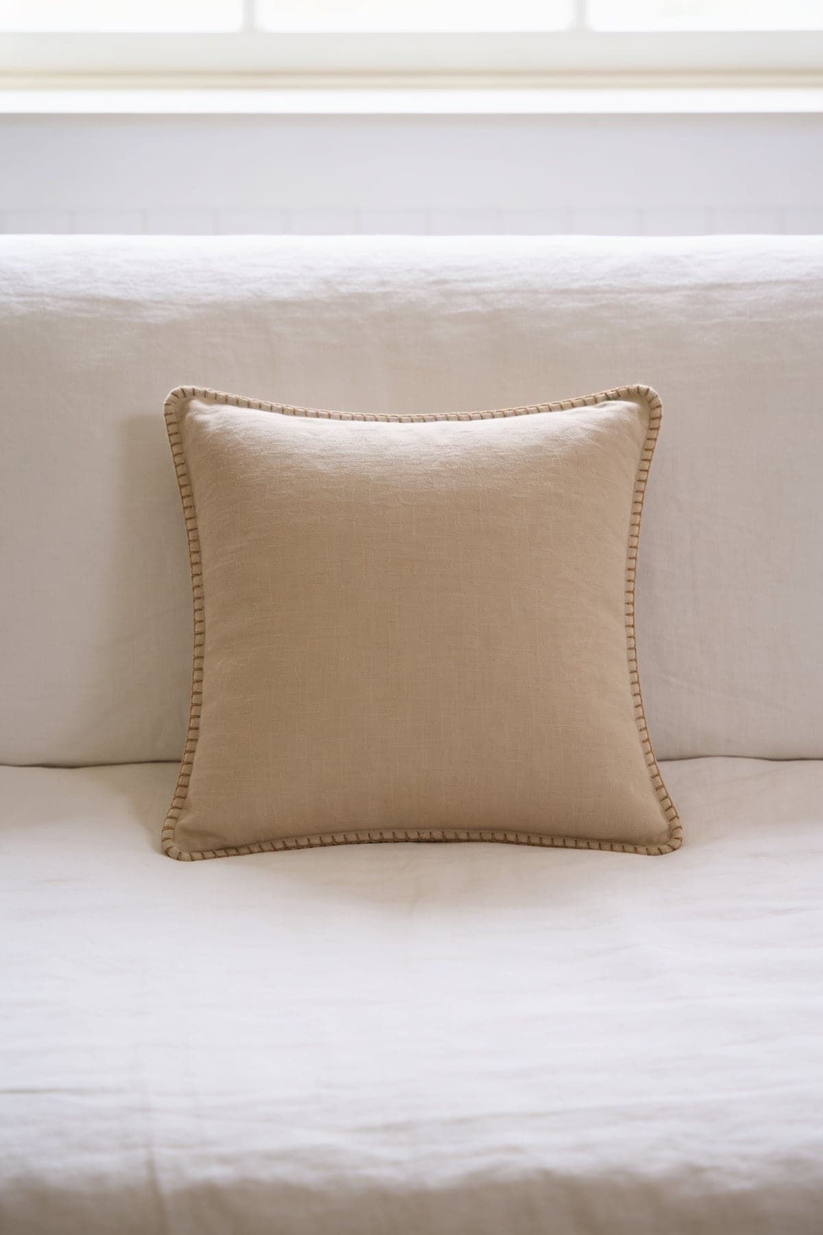 A beige linen cushion with a contrast stitched edge on a white linen sofa