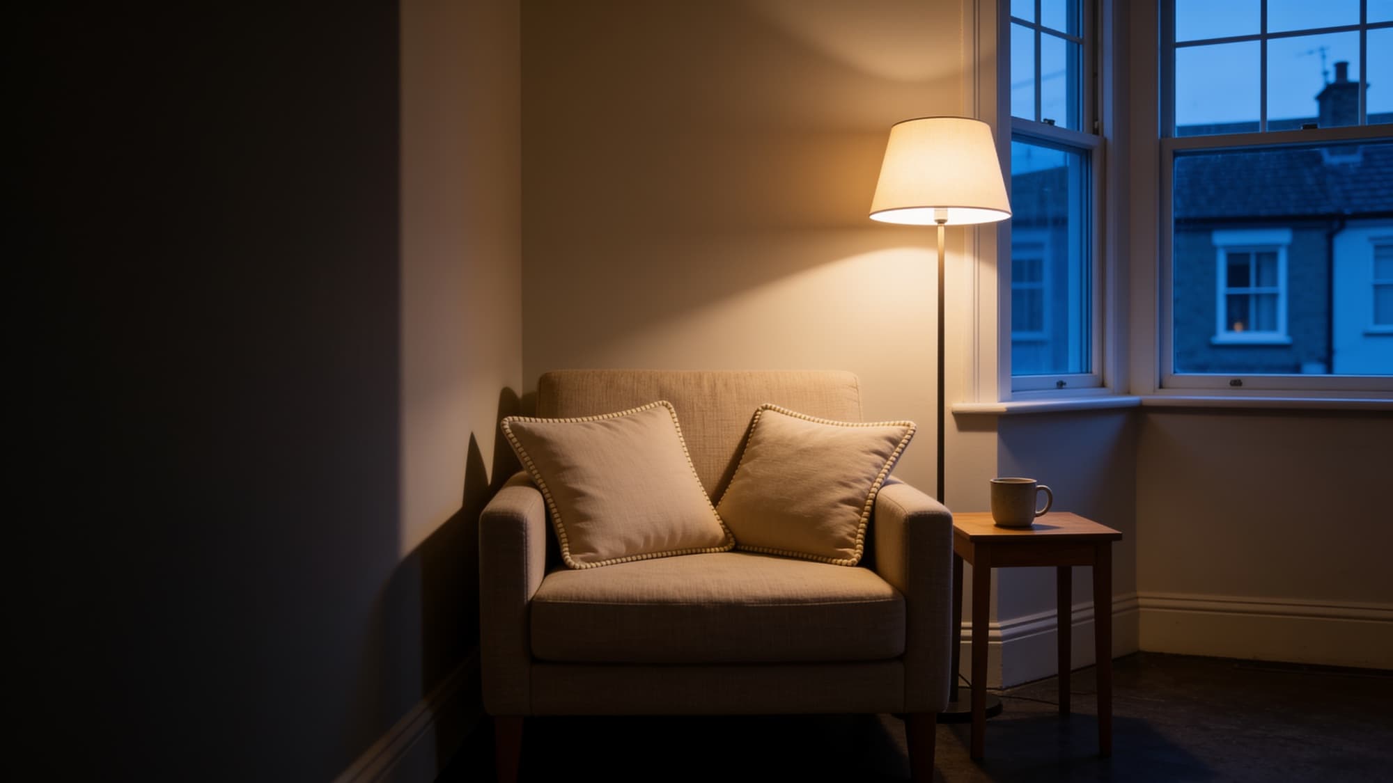Two beige linen cushions on a linen sofa under a floor lamp at dusk