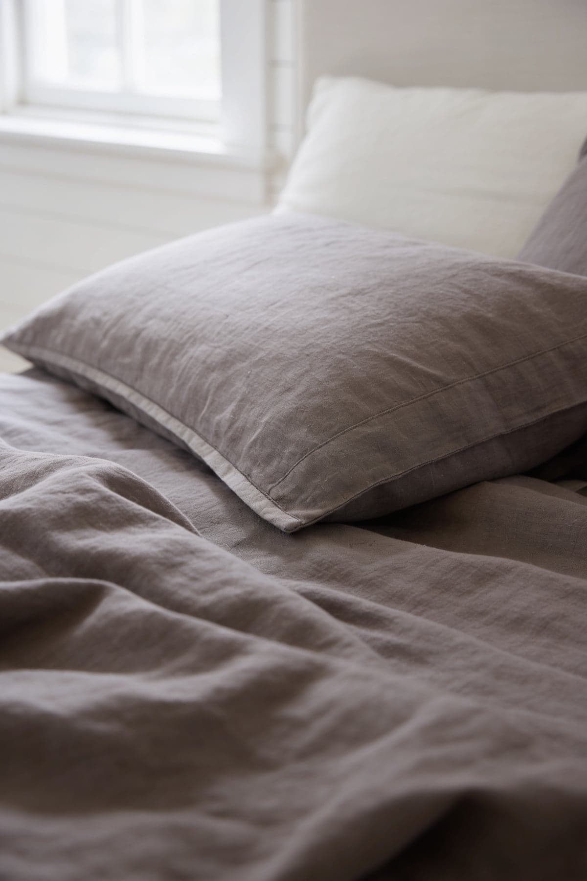 Close up of the grey-brown stonewashed linen pillowcase and duvet in soft daylight