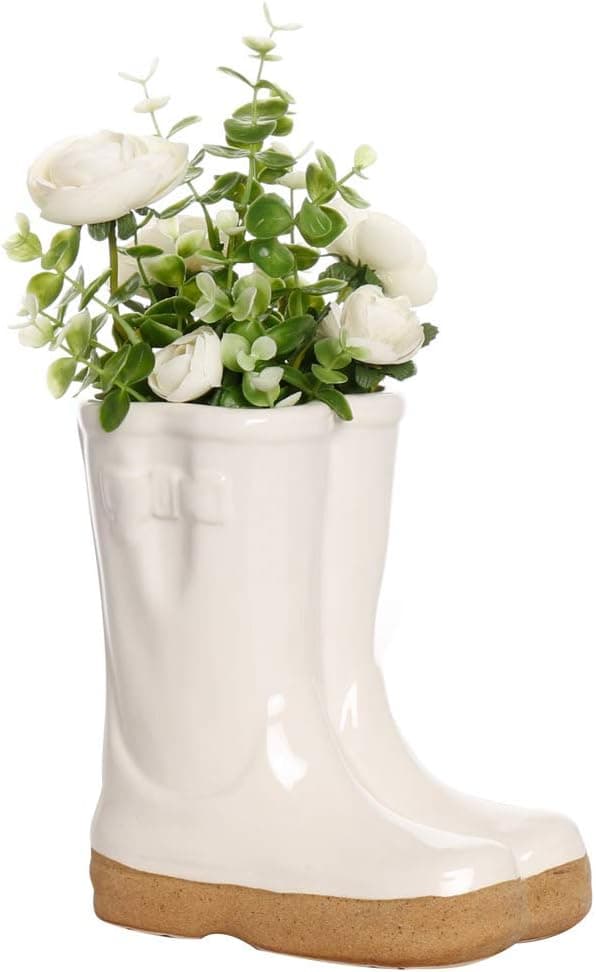 A white glazed ceramic planter shaped like a pair of wellington boots, planted with white roses and greenery
