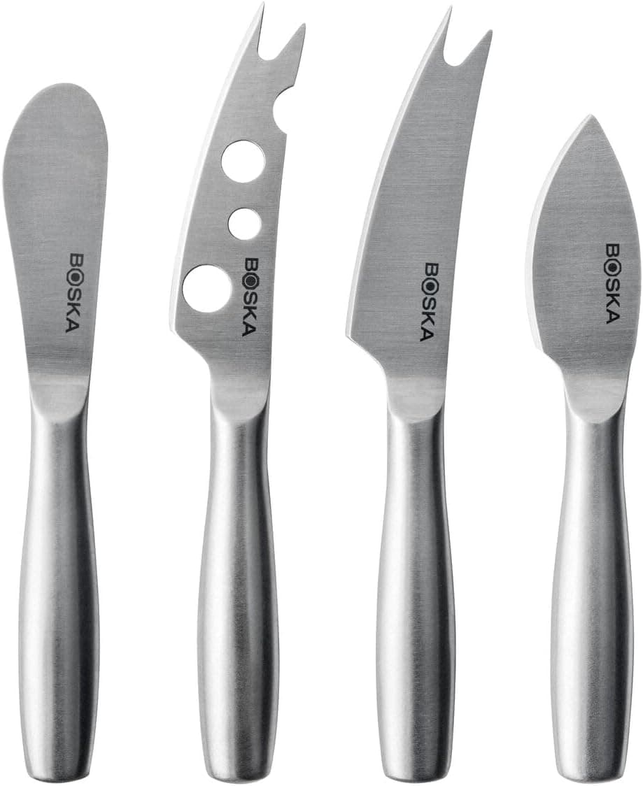 Four small cheese knives in plain brushed stainless steel, each with a different blade shape, laid side by side