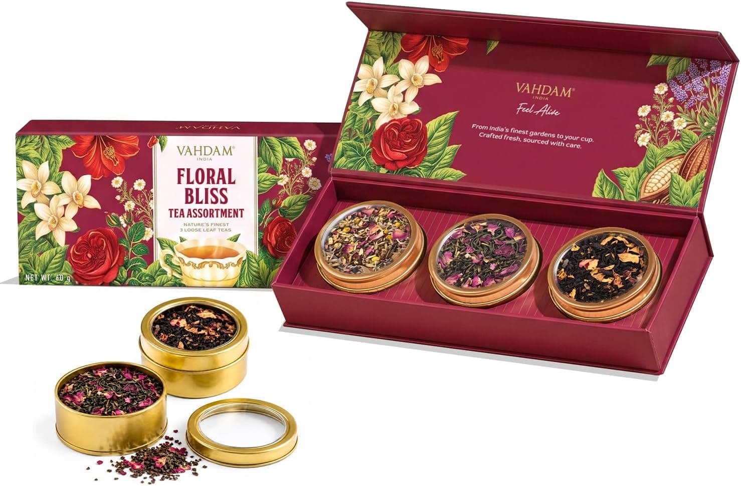 Three small gold tea caddies in a floral presentation box, open on a kitchen table beside a teapot and a strainer