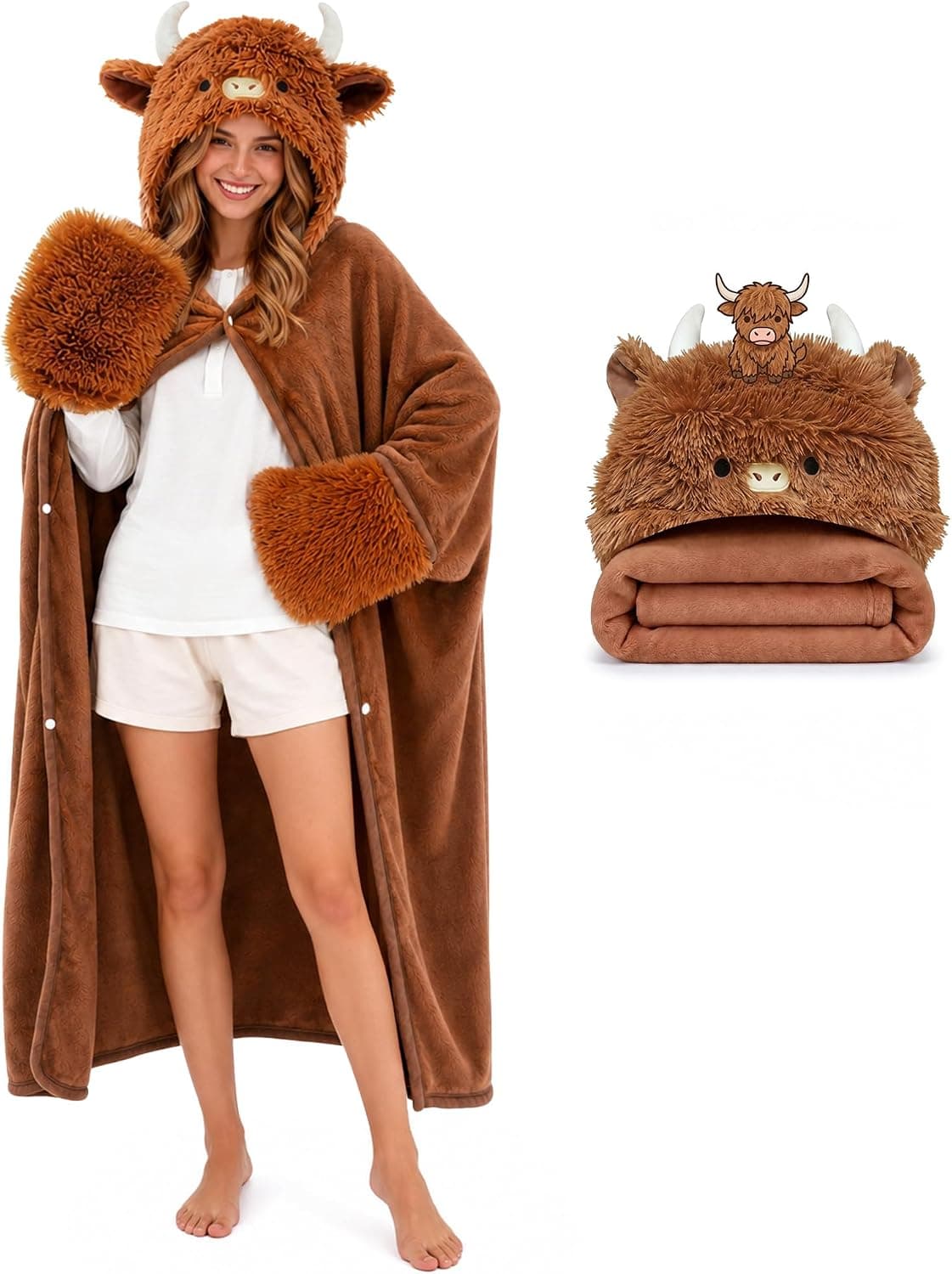 A person on a sofa wrapped in an oversized cream hoodie blanket with a highland cow face on the hood, holding a mug