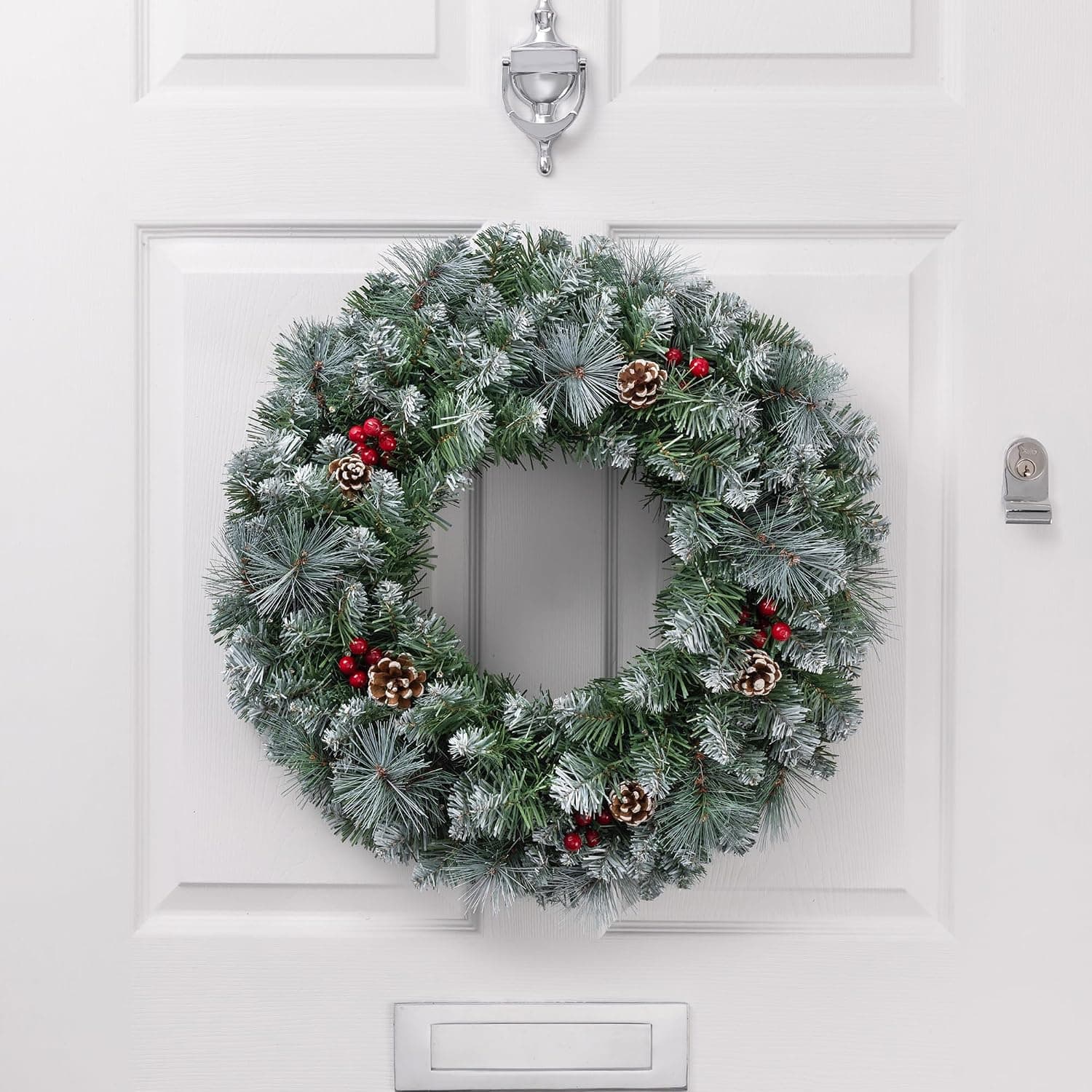 A full 60cm green pine wreath with white-frosted tips, pine cones and red berries on a white panelled front door