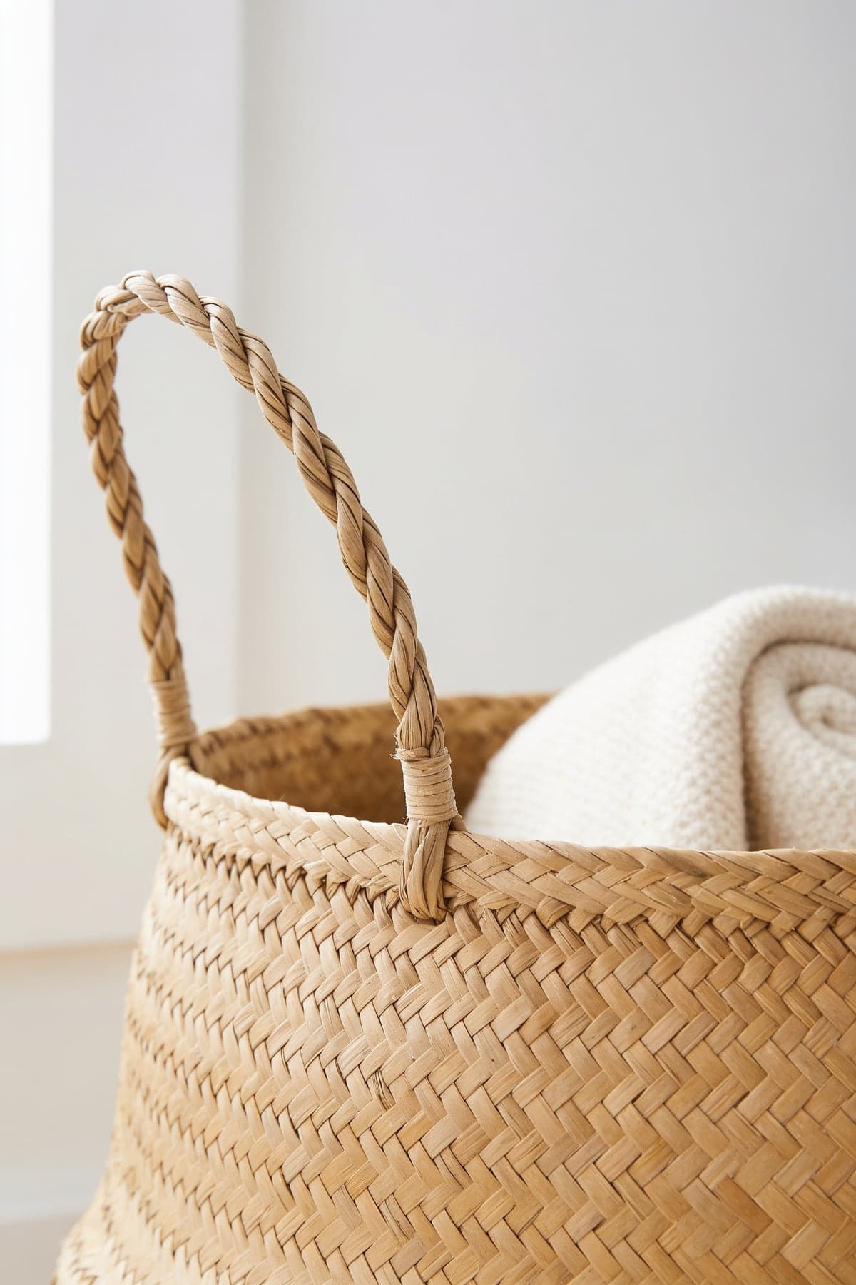 Close up of the seagrass basket's woven body and plaited handle, a throw rolled inside