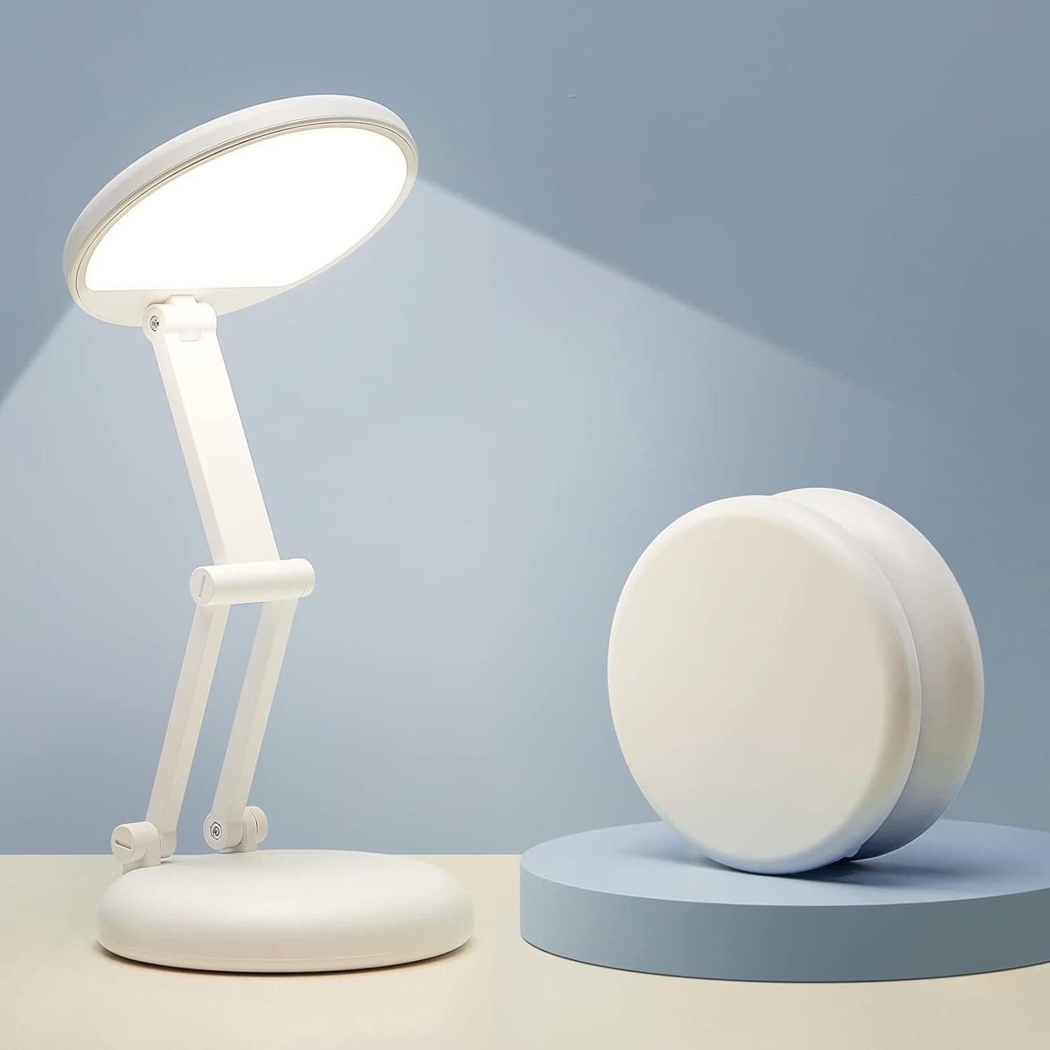 A small white cordless LED lamp with a round shade on a folding stem and a round base