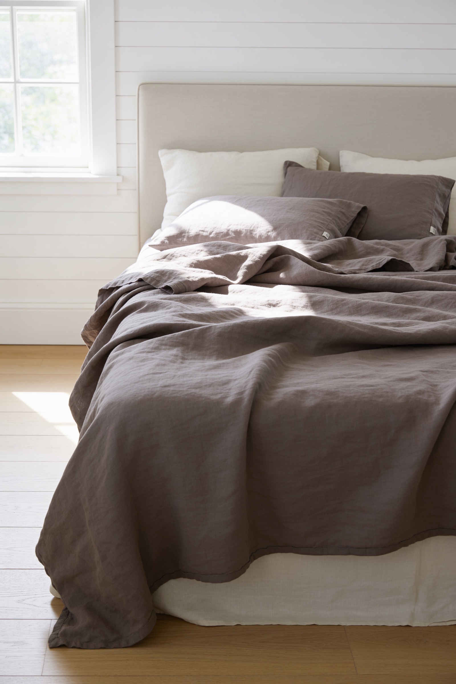 Stonewashed taupe linen duvet on a sunlit summer bed with a soft, lived-in crumpled texture